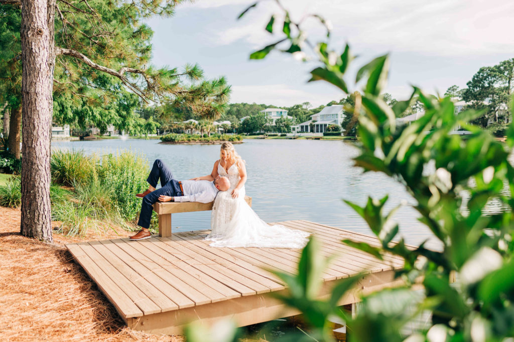 groom lounges with head on bride's lap on a bench by the water at Sandestin resort in Miramar Beach Florida