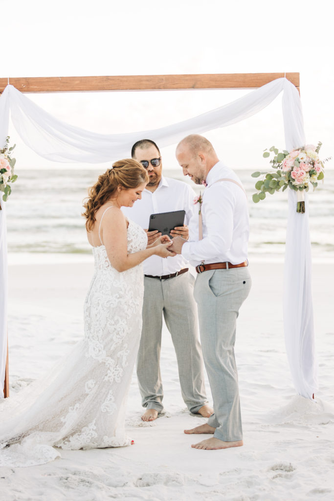 bride puts on groom's ring during wedding ceremony on Miramar Beach