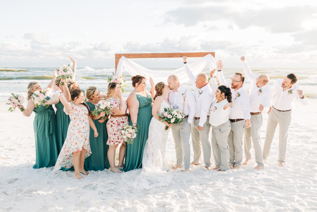 wedding party cheers as bride and groom kiss after ceremony on Miramar Beach Florida