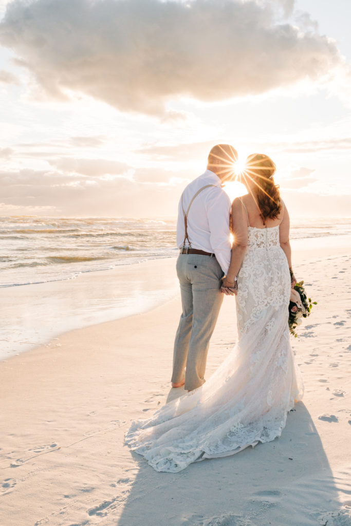 bride and groom kiss on Miramar Beach with sunburst from sunset