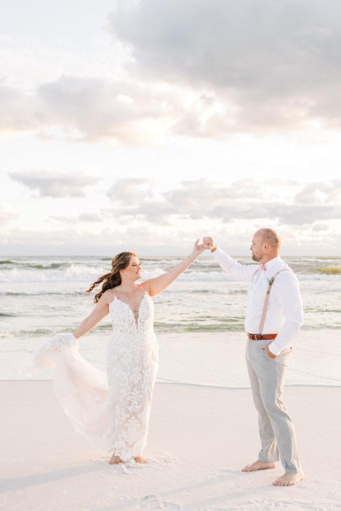 Groom twirls bride while smiling in front of gulf on Miramar Beach for wedding photo