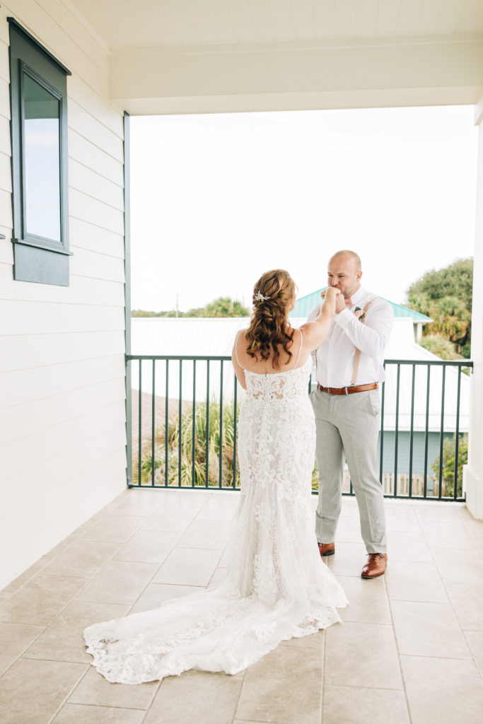 groom kisses bride's hand after first look on porch of beach house in Destin, Florida