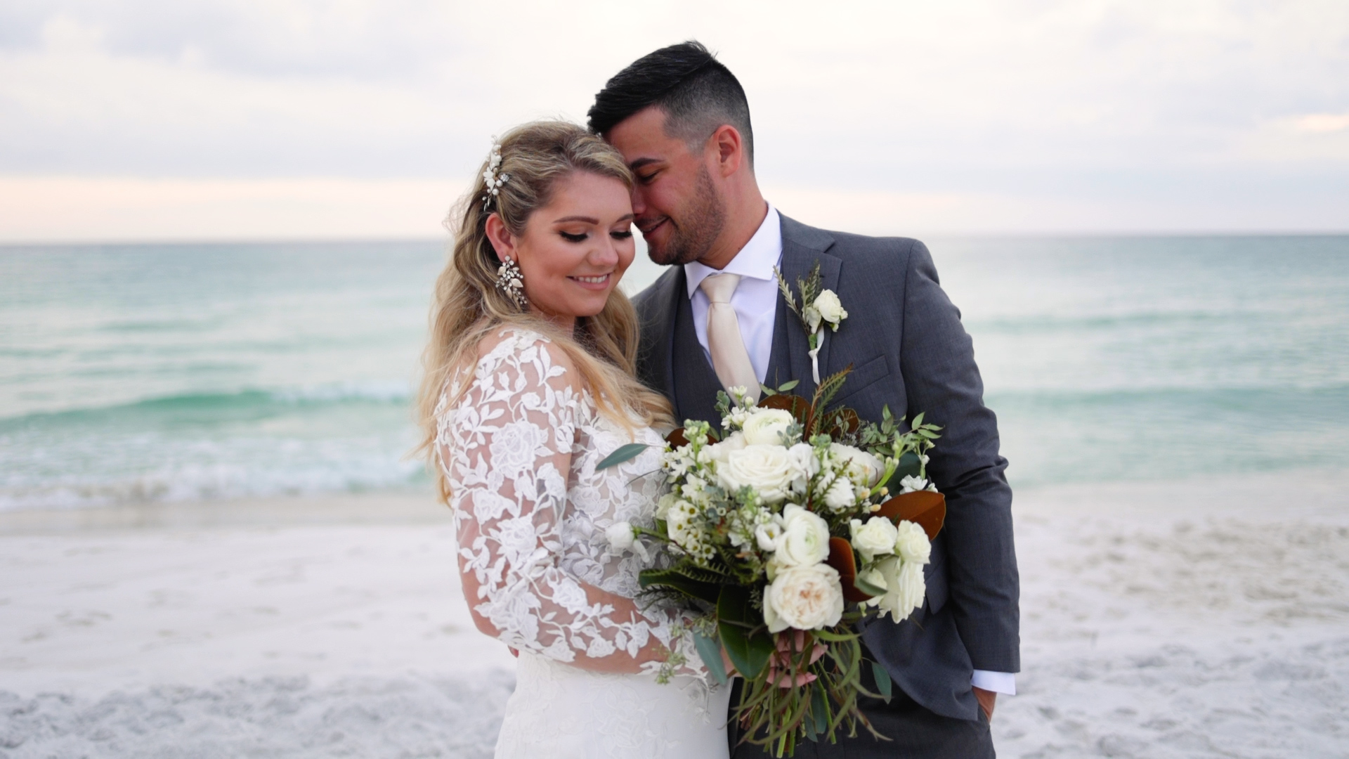 bride smiles at bouquet while groom hugs her on grayton beach after their wedding at monet monet